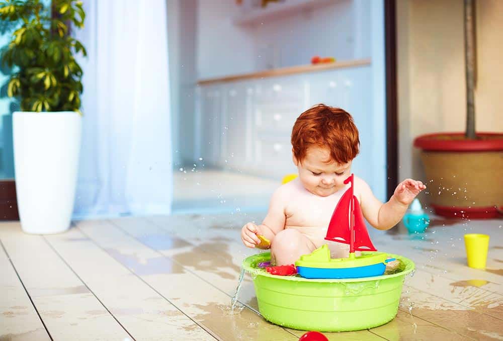 redhead toddler in a green plastic portable tub with a sailboat