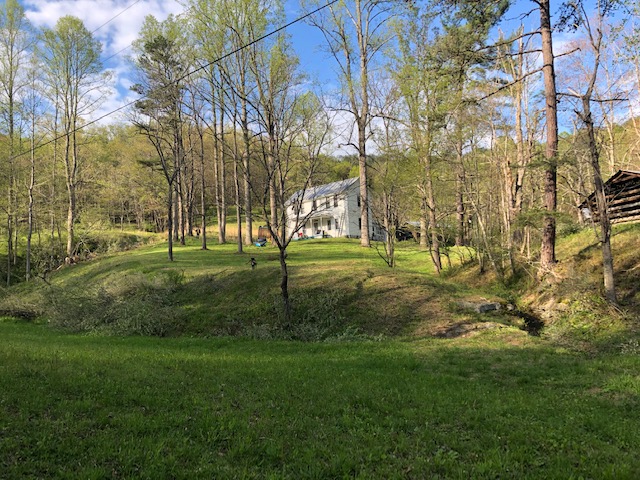 an old white farmhouse on a wooded hill. A log outbidding is visible on the right. 