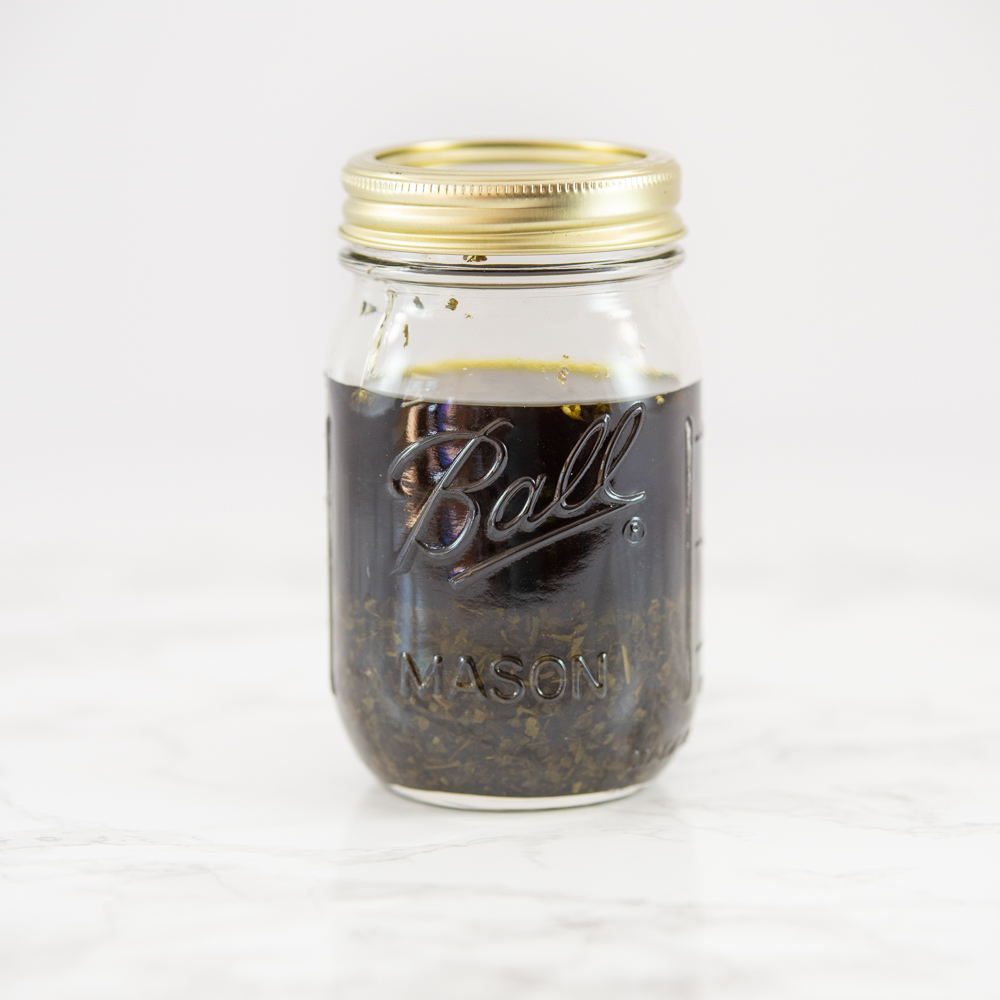 A pint Ball mason jar of homemade mint extract. There are mint leaves visible at the bottom and the liquid is green.