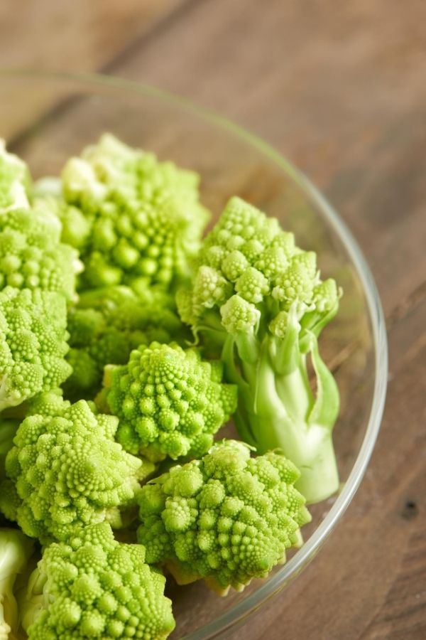 A bowl of cut Romanesco broccoli florest in a glass bowl on a wood table