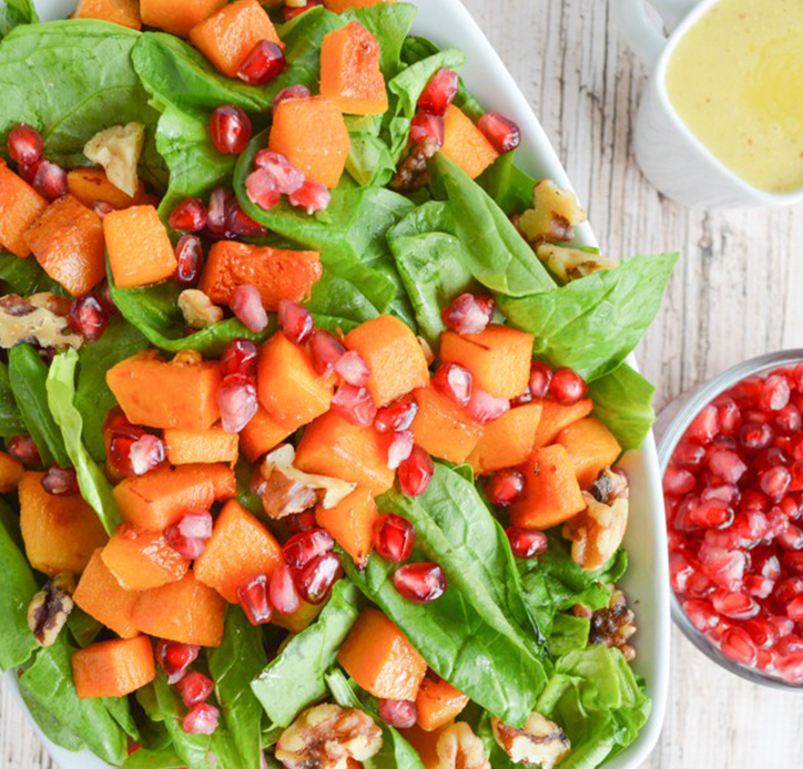 a closeup of a salad comprised of baby spinach leaves, butternut squash cubes, and pomegranate seeds