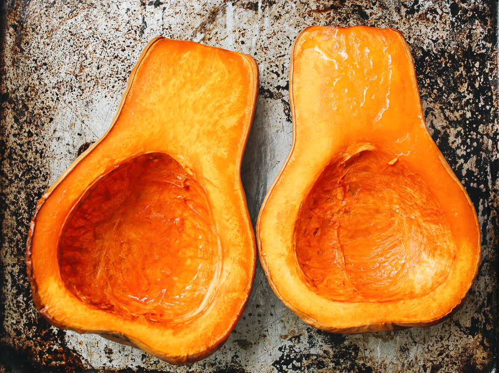 Two cut open and roasted halves of a butternut squash on a baking sheet.