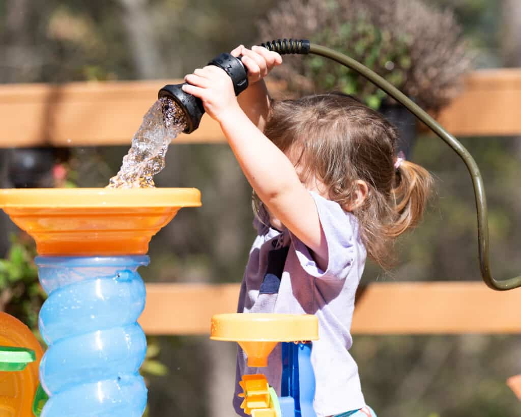 A young child using a fireman hose nozzle to fill a water table