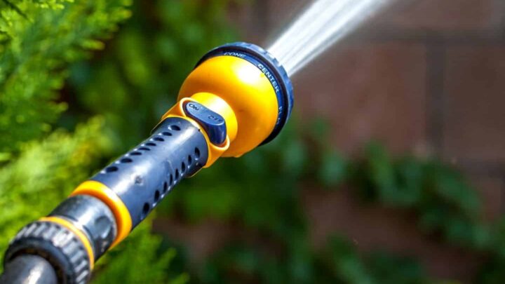 Text reads "The best high pressure hose nozzles" on a translucent white box at the bottom of the image. There is an orange and black hose nozzle spraying a thick stream of water at high pressure at an out of focus brown and green background.