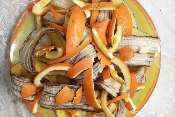 A top down view of cut banana peels and orange rinds in a shallow yellow and orange bowl