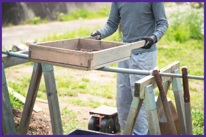 A man using a stand-p soil sifter resting on a pair of saw horses