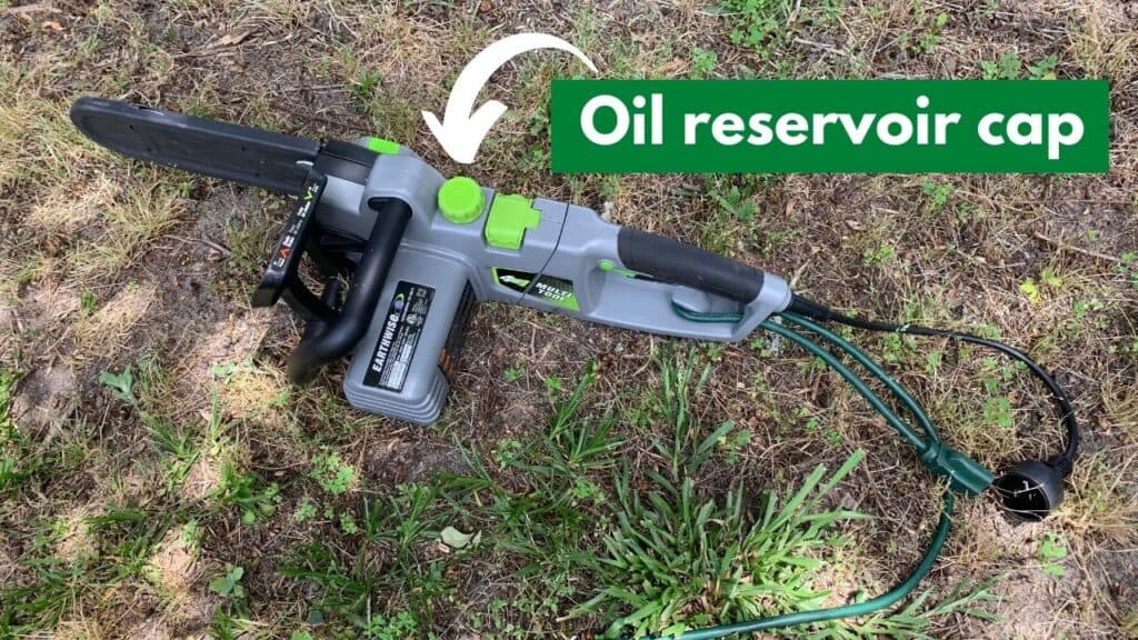 Text reads "oil reservoir cap" in a green text box with a white arrow pointing to the oil reservoir cap on the earthwise 4 in 1 multi tool chainsaw. The tool is on a grassy patch, sitting on the ground.