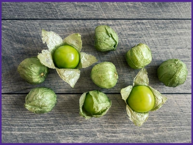 Nine green tomatillos on a wood table