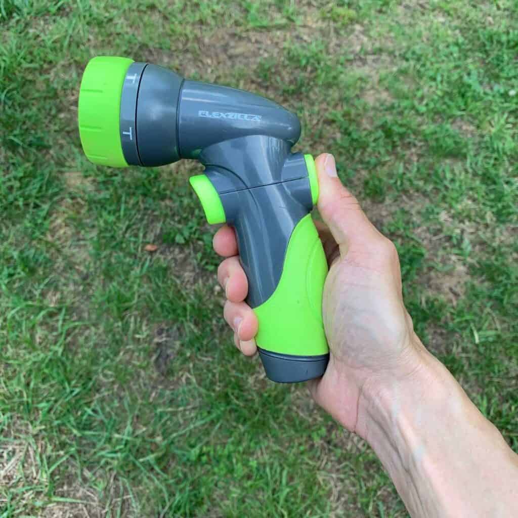 A woman's hand holding a grey and chartreuse green Flexzilla pattern hose nozzle