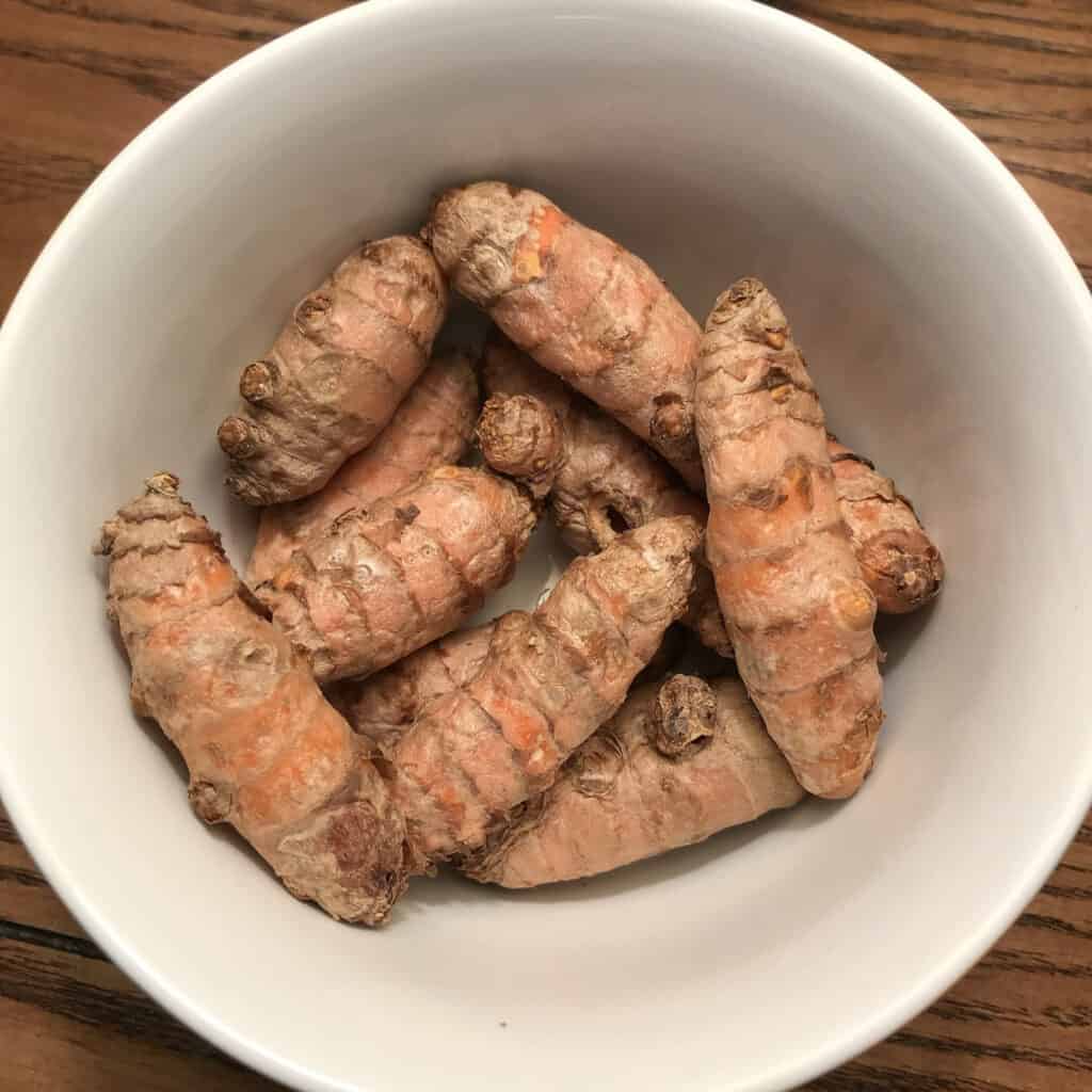 A top down view of a small white bowl with turmeric rhizomes
