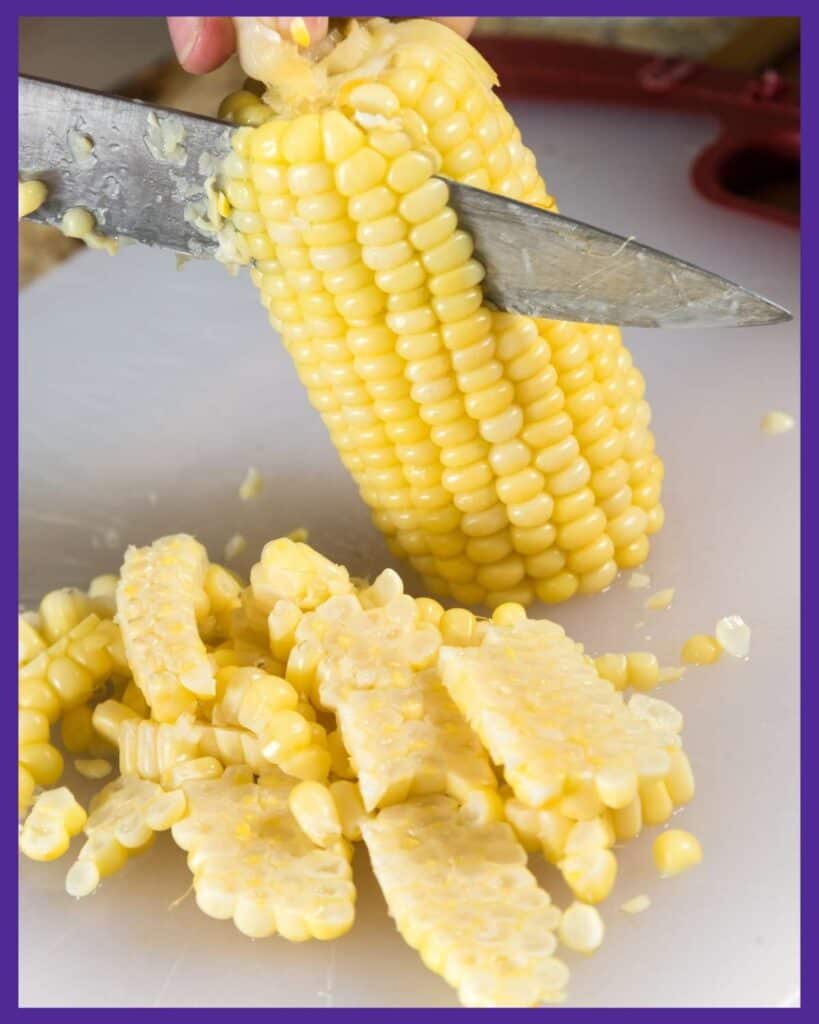 A close up image of a person cutting corn off the cob with a large knife