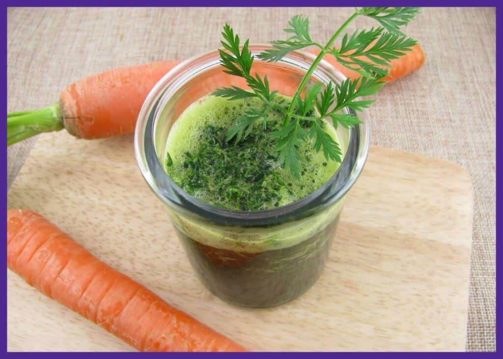A top down photo of a green smoothie with two carrots on a cutting baord