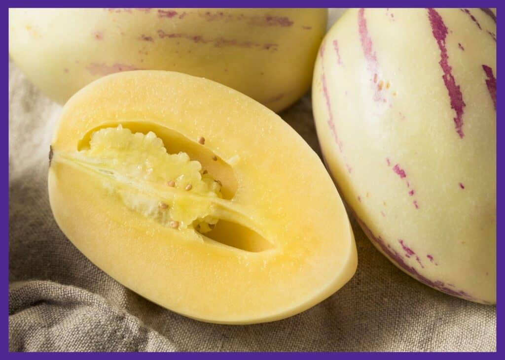 A cut open pepino melon. It has a yellow skin with purple stripes. The inside has yellow flesh.