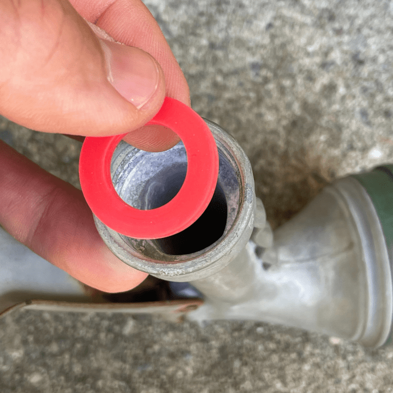 Photo is of the underside of a hose nozzle and a red hose washer being placed into the inlet.