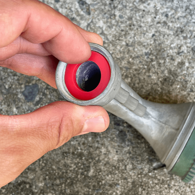 Photo is of a red hose washer being placed into a hose nozzle. The person is using their index finger to push in the washer.