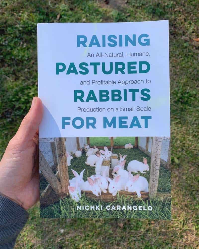 A hand holding the book Raising Pastured Rabbits for Meat