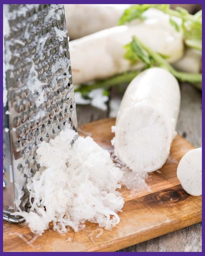 Grated horseradish next to a metal box grater on top of a wood cutting board