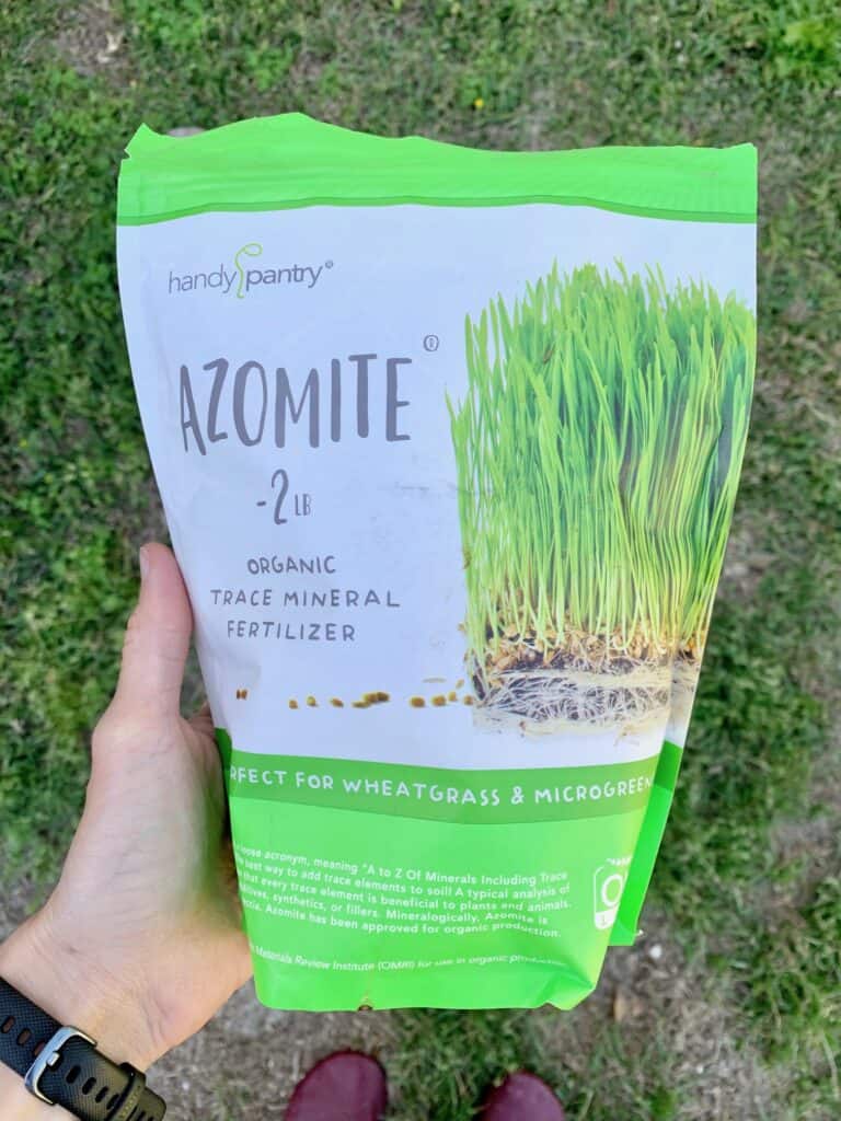 A hand holding a 2 lb bag of Handy Pantry brand Azomite organic fertilizer