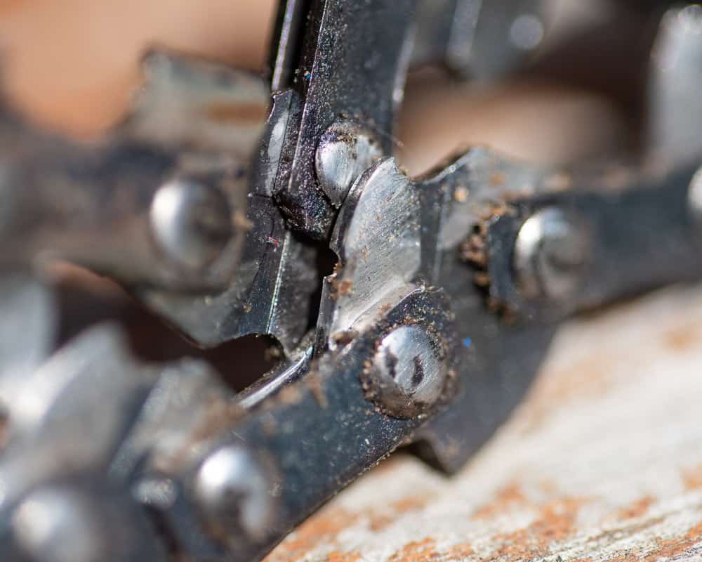 Photo is of a dirty chainsaw chain with dirt between the links and a large gouge in the drive link.