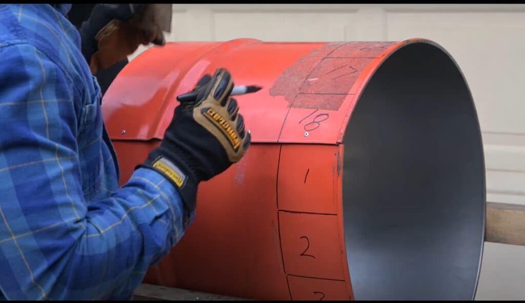 Photo is of a man labelling squares 1 through 18 on a half of a 55 gallon drum.