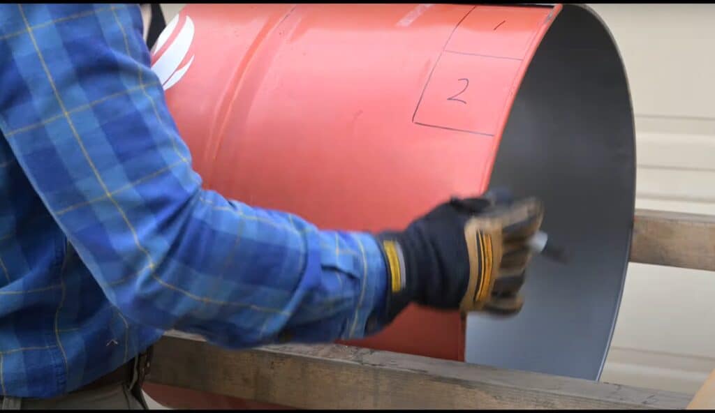 Photo is a man labeling squares on a 55 gallon drum to make vents and legs.