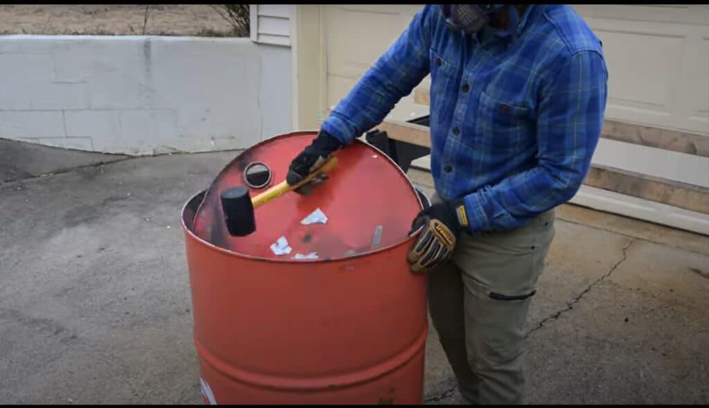 Photo is of a man removing the lid from a 55 gallon drum after grinding off the lid.