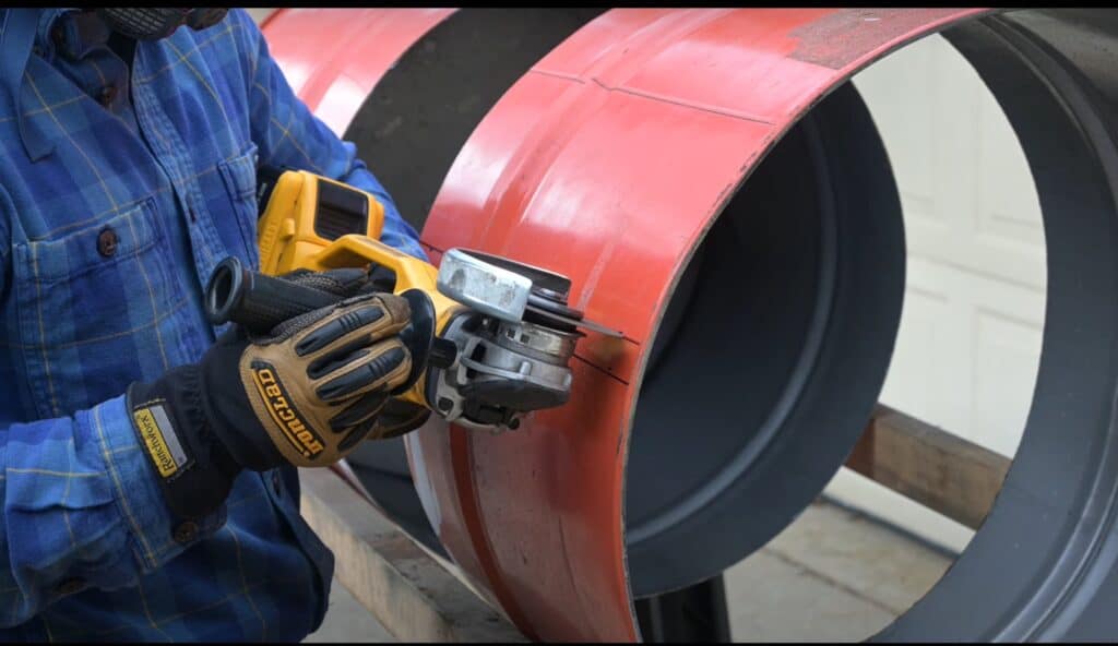 Photo is of a man cutting a line on a 55 gallon drum using a yellow angle grinder.