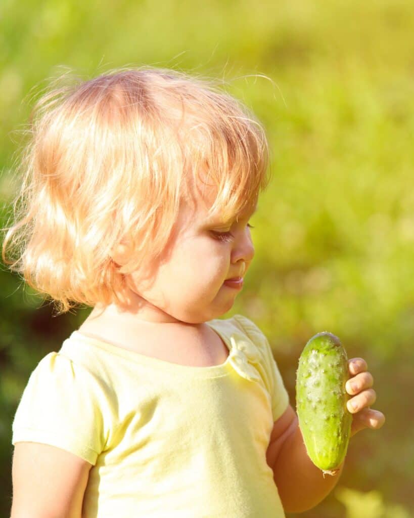 a young girl holding a cucumber