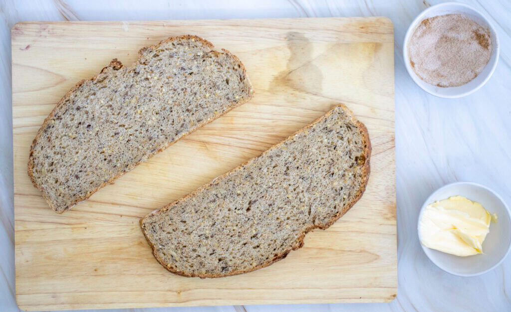A wooden cutting board displays two slices of sourdough bread alongside bowls of butter and a brown sugar mixture, suggesting various toppings for sweet or breakfast sourdough toast ideas.