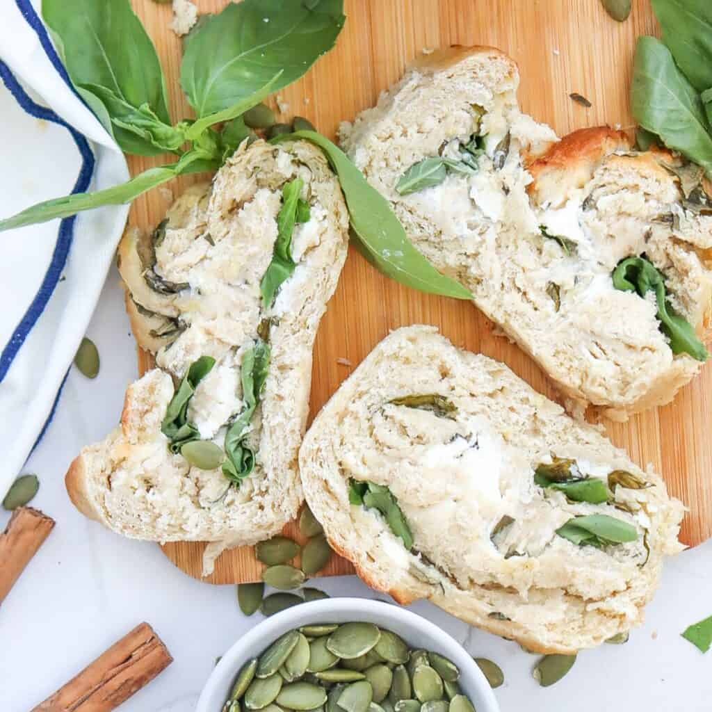 a cutting board with four slices of zucchini swirl bread with pumpkin seeds and basil