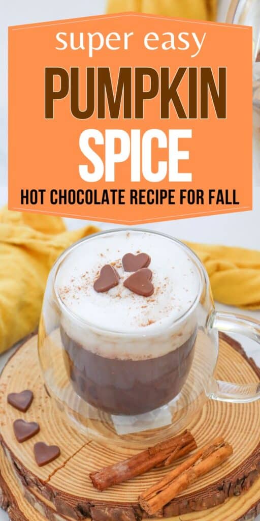 A clear glass mug filled with pumpkin spice hot chocolate, topped with whipped cream and chocolate hearts, sits on a wooden coaster alongside cinnamon sticks and a soft yellow cloth in the background, featuring text about a fall hot chocolate recipe.
