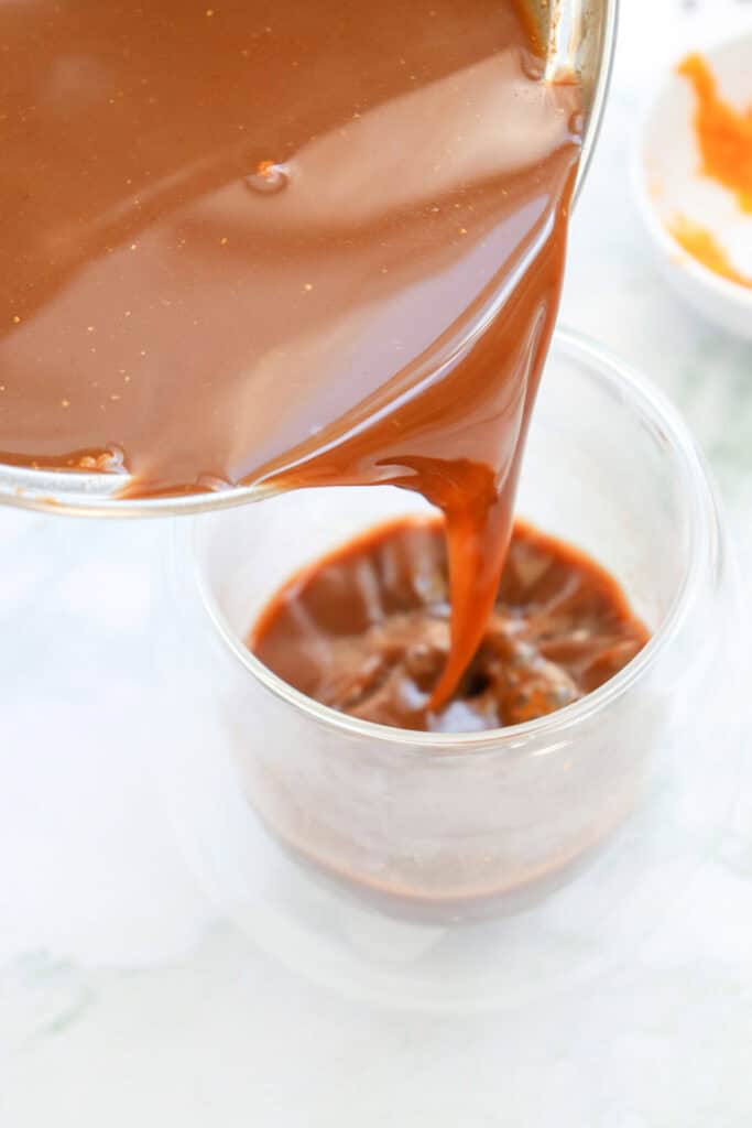 A glass is being filled with a rich pumpkin hot chocolate mixture, highlighting fall hot chocolate recipes and pumpkin spice hot chocolate ideas.
