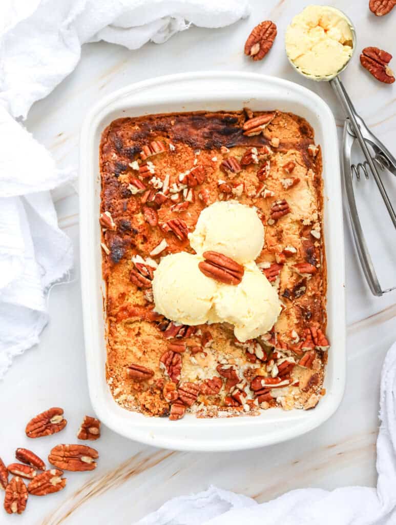 A pan of gluten free pumpkin spice dump cake with pecans and ice cream on top