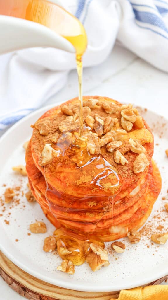 A stack of pumpkin pancakes topped with walnuts and drizzled with syrup, ready to be enjoyed as part of an easy autumn breakfast.
