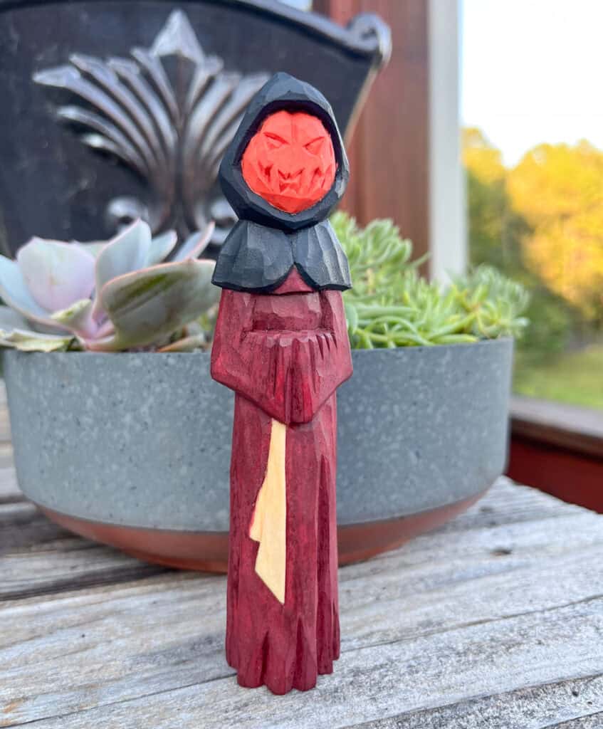 a wood carved halloween figure with a jack o lantern face