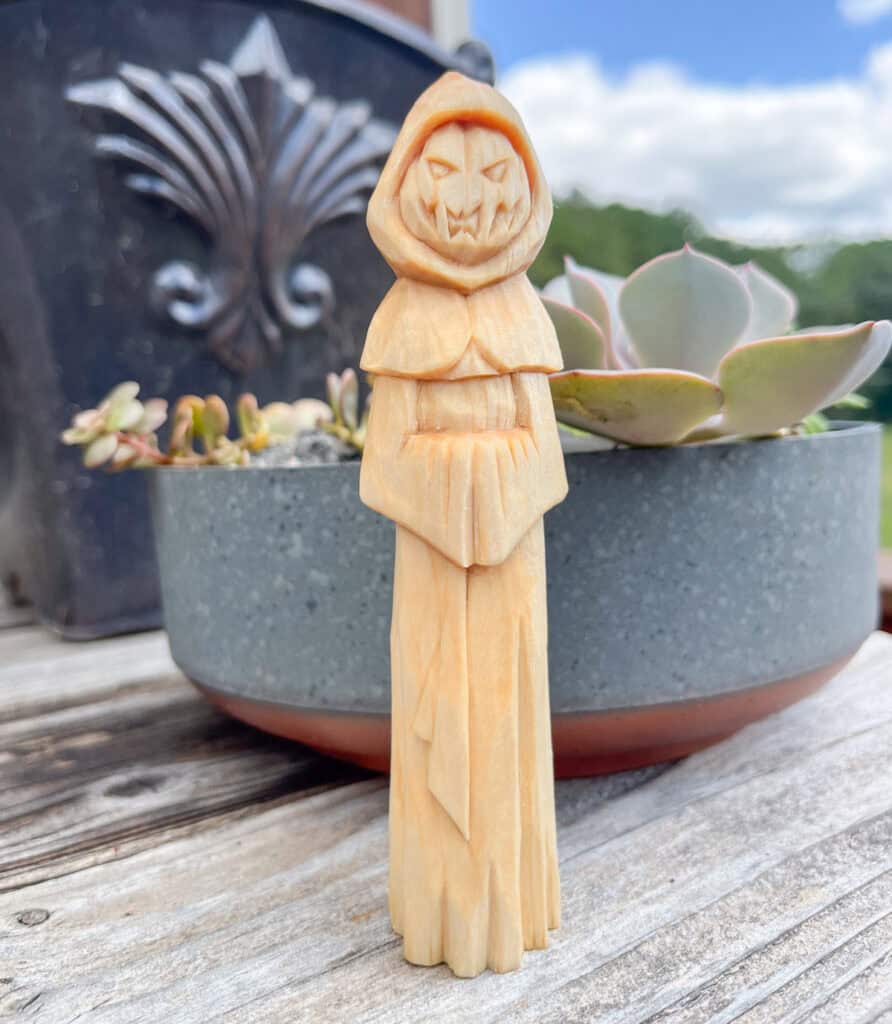a wood carving of a creepy Halloween figure with a robe and jack o lantern face