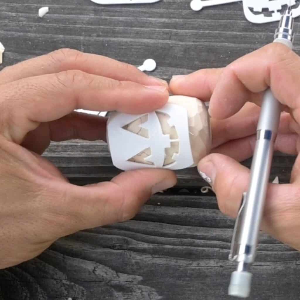 holding a flexible jack o lantern face stencil onto a block of wood